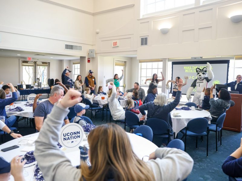 People in UConn gear at the Alumni Center Great Hall doing a UConn chant in unison