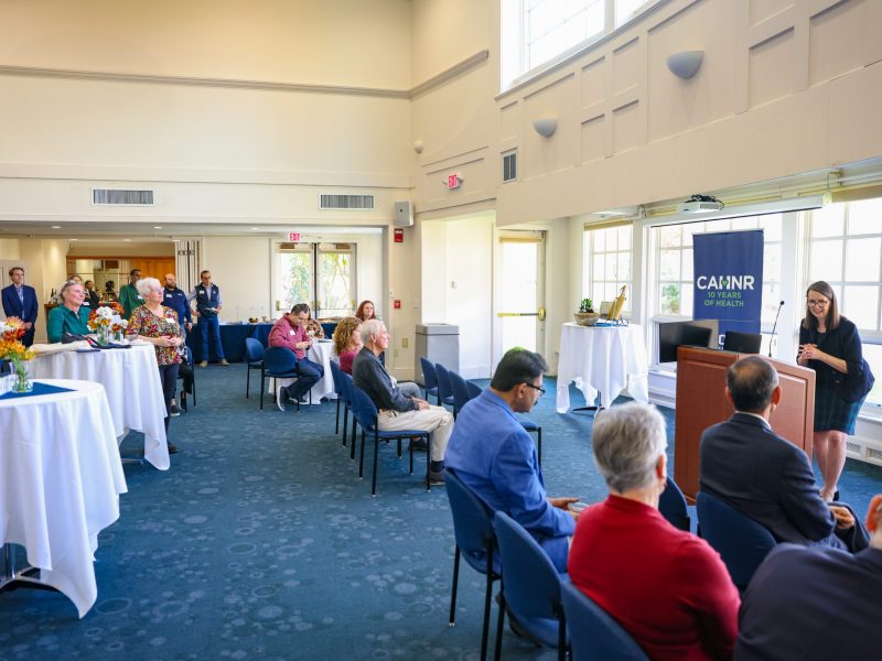 A speaker at a podium in the Alumni Center Great Hall with an audience watching from chairs and tables