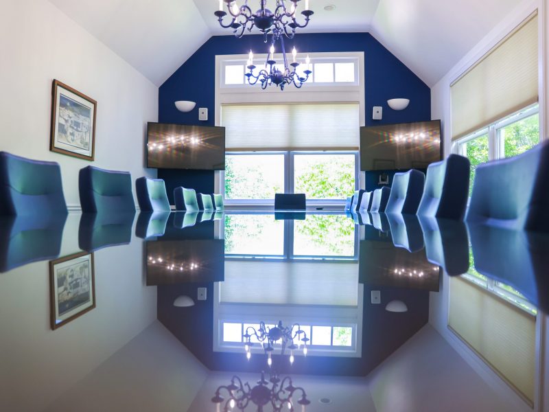 The Alumni Boardroom featuring high ceilings with chandeliers, two televisions, a long table, and navy blue leather chairs