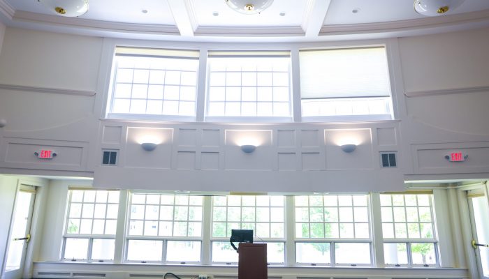 Facing the front of the Great Hall where a speaker podium is situated in the center, with large windows behind it