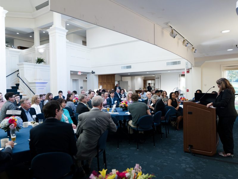 Award recipients from the CLAS Alumni Awards, sitting at tables in the Great Hall, looking towards the podium with someone presenting.