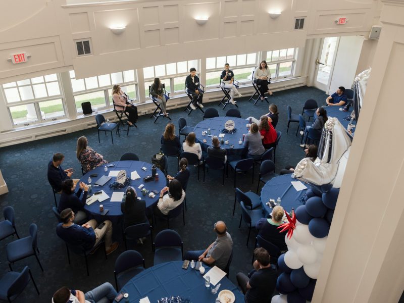 An aerial shot of students speaking at a panel in the Great Hall, with Foundation employees sitting around them at tables.