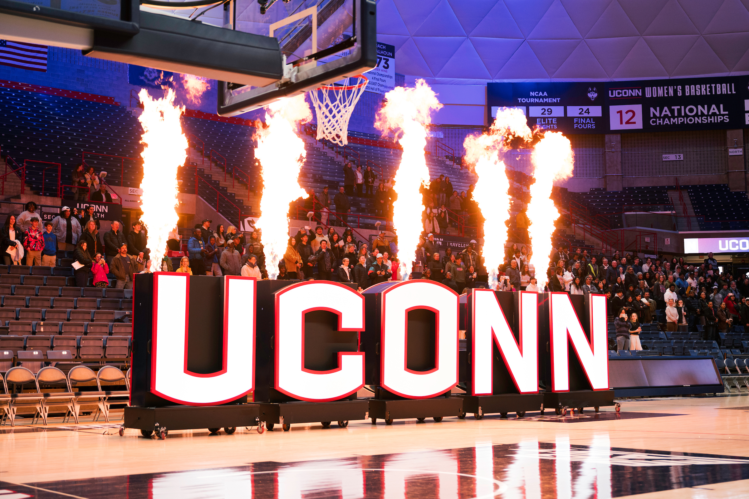 UConn sign on a basketball court with flames shooting up from each letter.