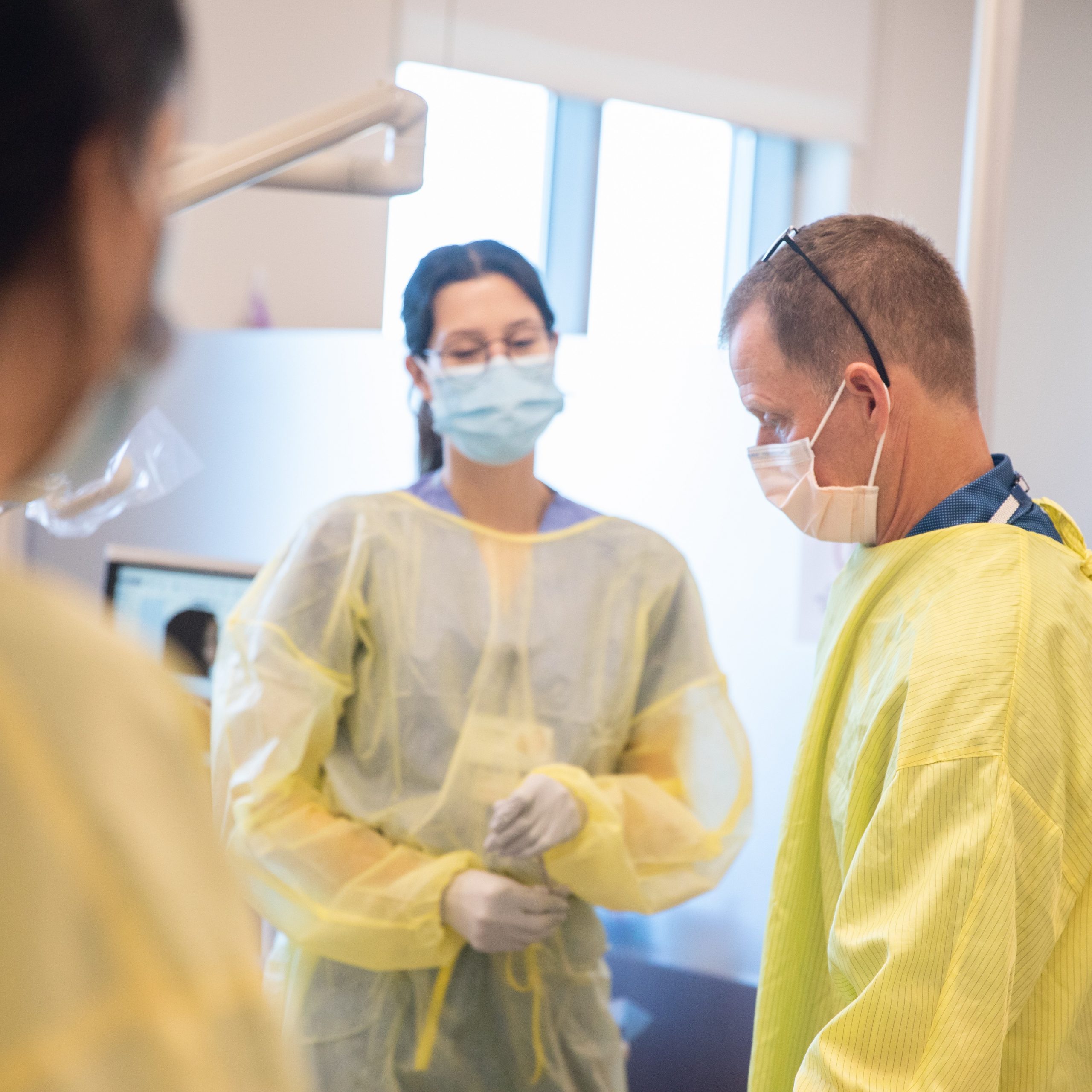 UConn Health Orthodontics Clinic with Dr. Jonathan Feldman featuring two other healthcare professionals wearing protective masks, gloves, and yellow gowns are gathered in a medical setting.