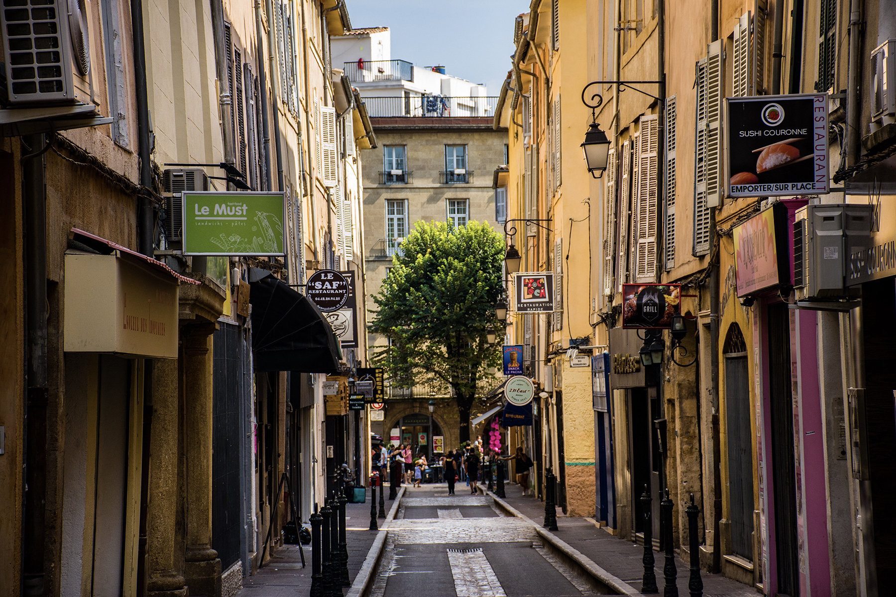 A narrow street in Aix-en-Provence, France, lined with tall, traditional European buildings featuring shuttered windows and light-colored facades
