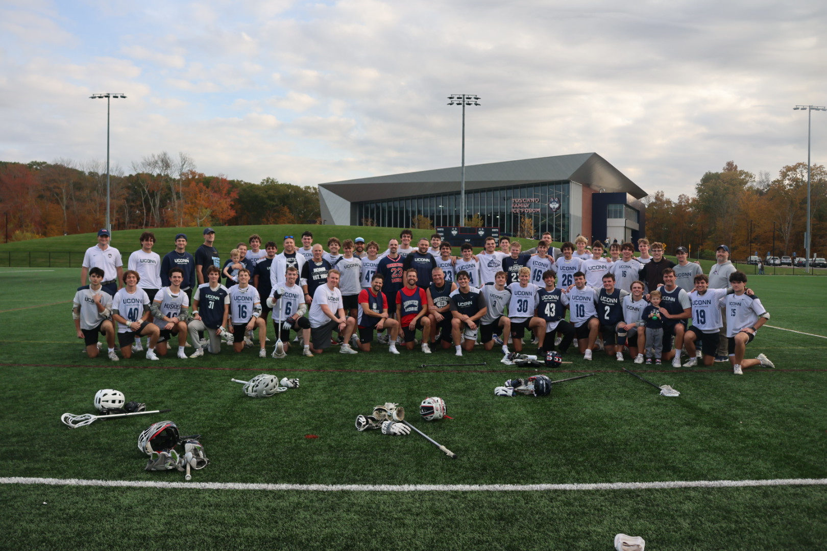 UConn men's lacrosse alumni posing for a picture on a turf field with their lacrosse gear on