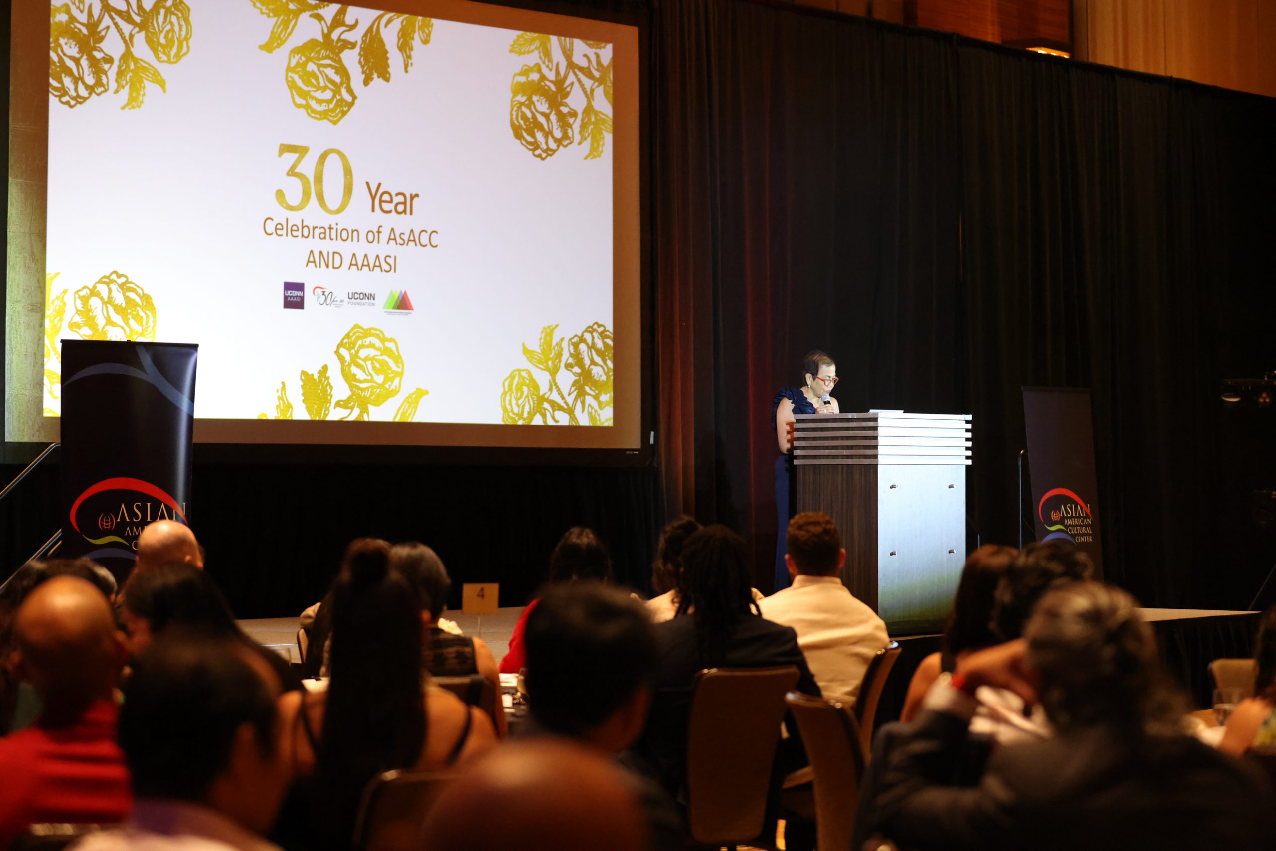 The Asian American Cultural Center 30th Anniversary Gala ballroom with people sitting down and watching someone speaking at a podium