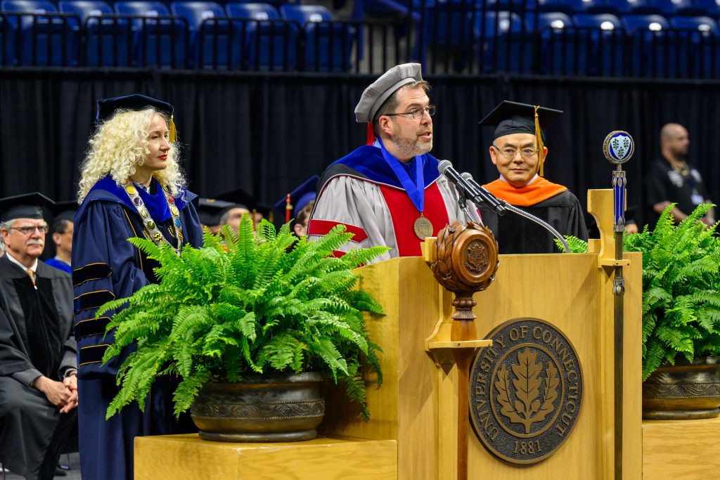 A faculty member standing at a podium and speaking during a graduation ceremony