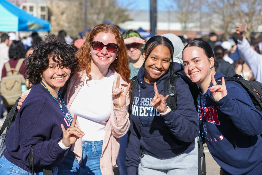 Students enjoying the 2024 Senior Send off event wearing UConn gear and putting up the "husky" sign with their hands