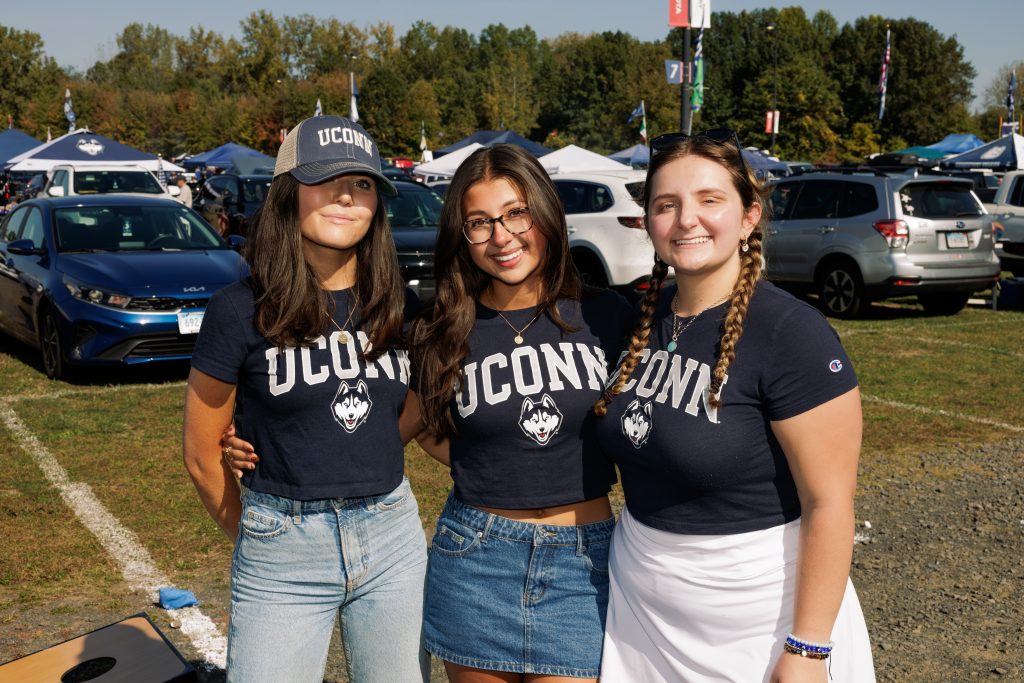 Three girls posting for a photo at the Homecoming Tailgate wearing UConn gear