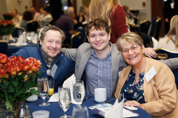 Three people smiling at a table with a flower bouquet