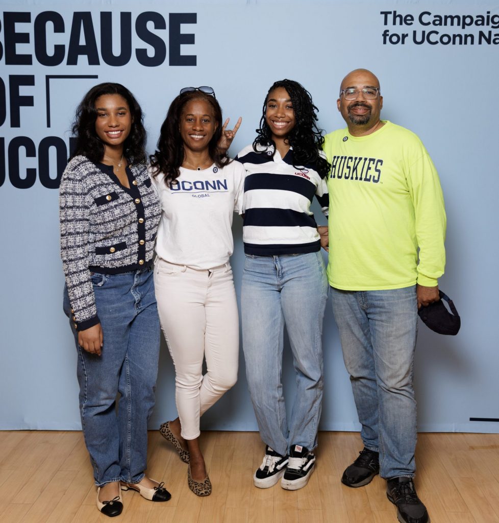 A family posing for a photo with a light blue "Because of UConn" backdrop at the 2025 Legacy Breakfast event