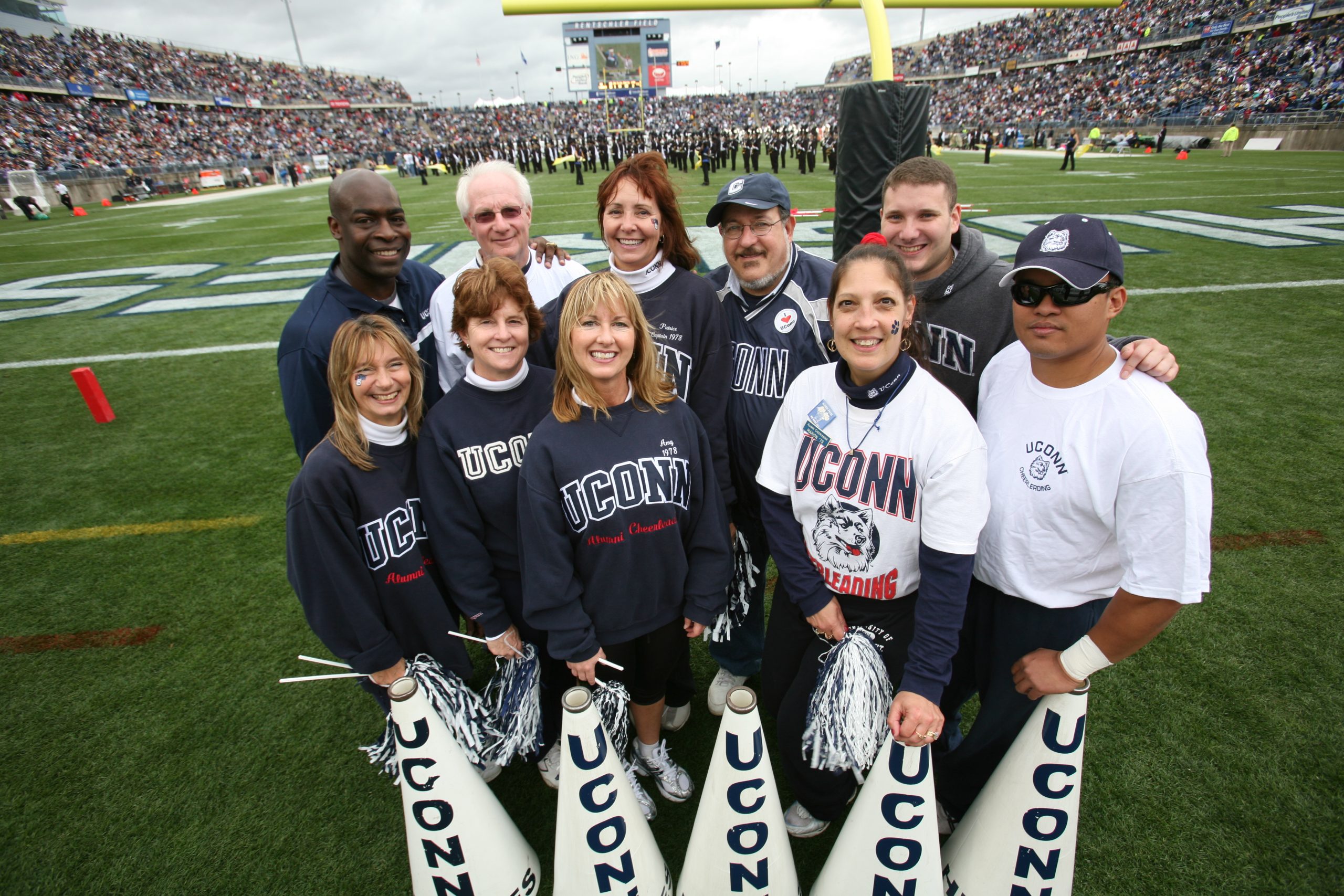 Alumni cheerleaders in their UConn gear on the football field at a homecoming game