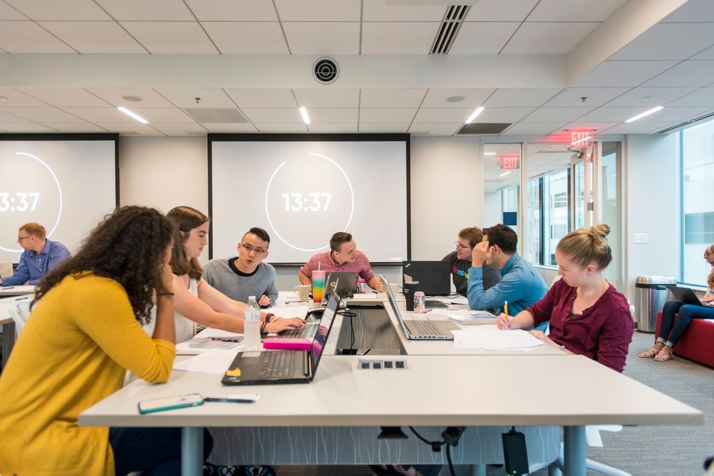 Students collaborating at a table with their laptops out and pens and paper