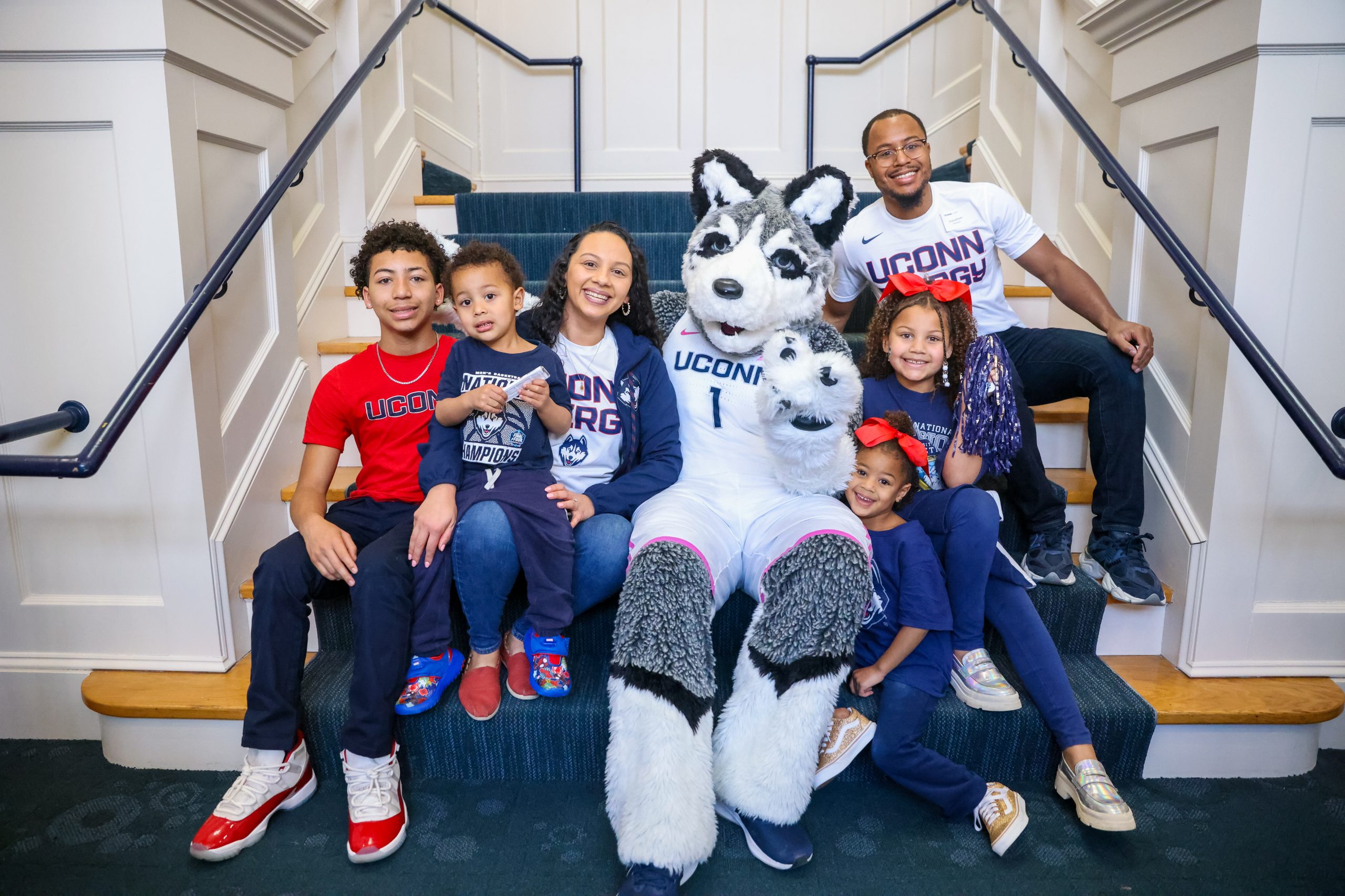 A family in UConn gear posing with Jonathan the mascot at the Meet and Sweet Family Event at the Alumni Center Great Hall