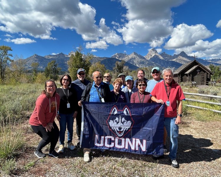 Alumni Grand Teton A group of travelers posing and holding up a UConn flag behind Grand Teton
