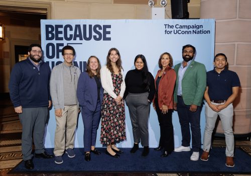 Because of UConn NYC The Because of UConn NYC event with attendees standing behind a photo backdrop