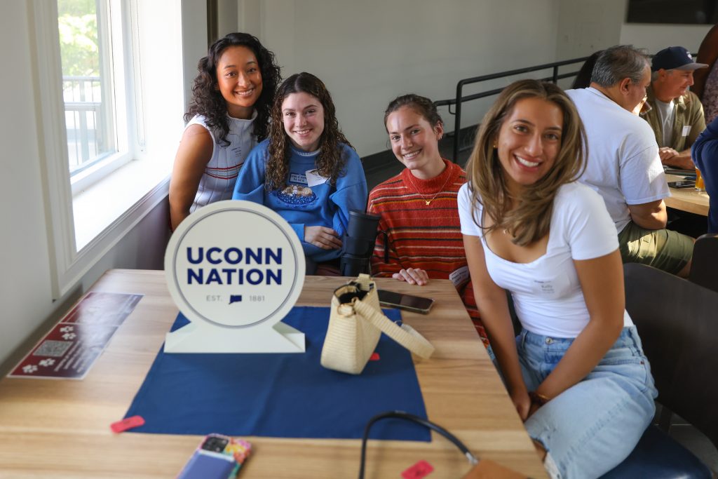 People posing for a photo at a table with a "UConn Nation" centerpiece at a Huskies In Your City event, held at Haven Beer Company