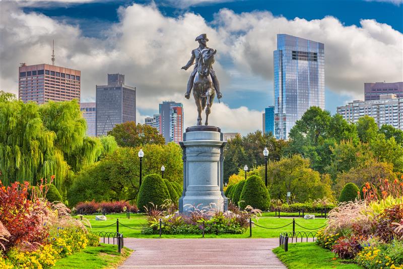 The statue of George Washington at the Boston Common featuring bright green plants and a skyline of the city
