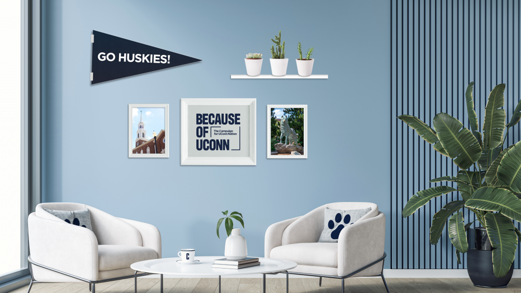 Light blue living room with UConn decor, framed photos, “Go Huskies!” pennant, plants, and two chairs with paw-print pillows.