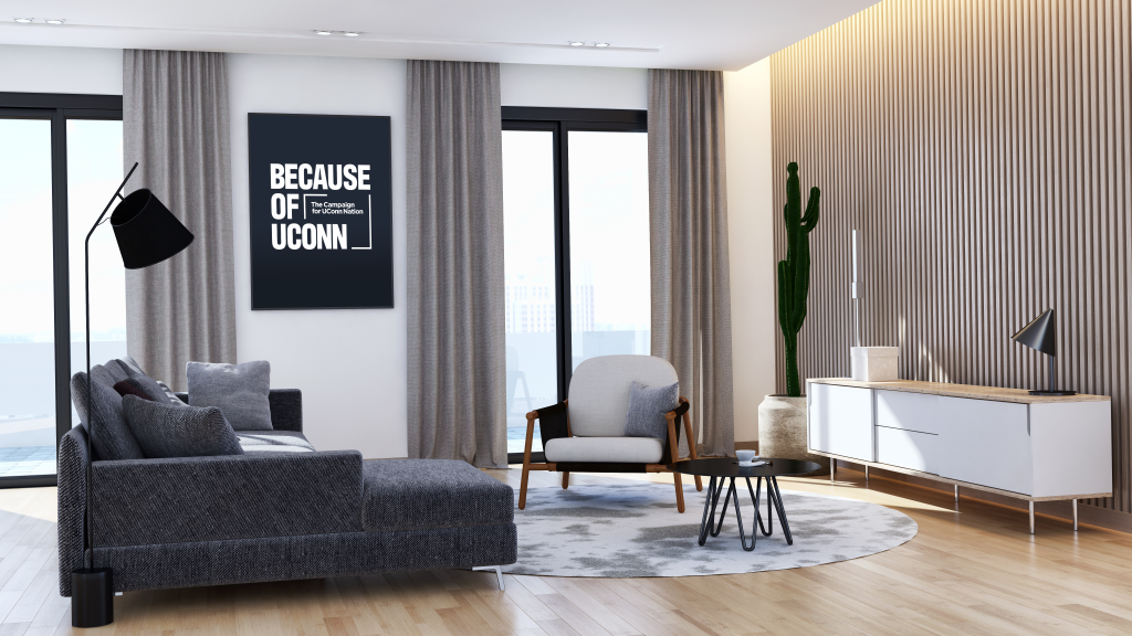Modern living room with gray sofa, armchair, round rug, and wall art reading “Because of UConn.” Large windows and a cactus add to the decor.
