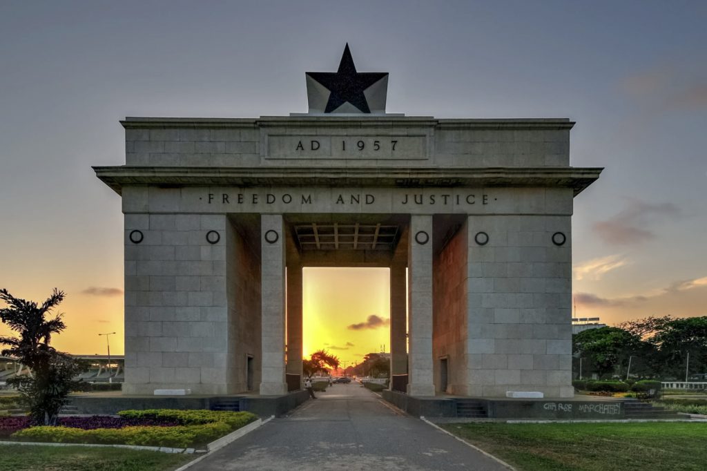Independence Arch in Accra, Ghana, with a black star on top and the inscription ‘AD 1957 – Freedom and Justice,’ photographed at sunset with the sun shining through the central opening.
