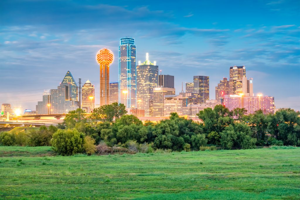 Skyline of downtown Dallas lit up with green park in the forefront