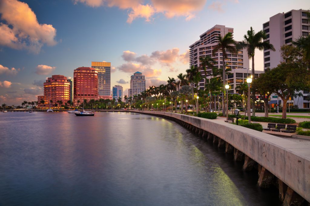 Skyscrapers line the waterfront in West Palm Beach, Florida, reflecting soft, golden hues from the setting sun