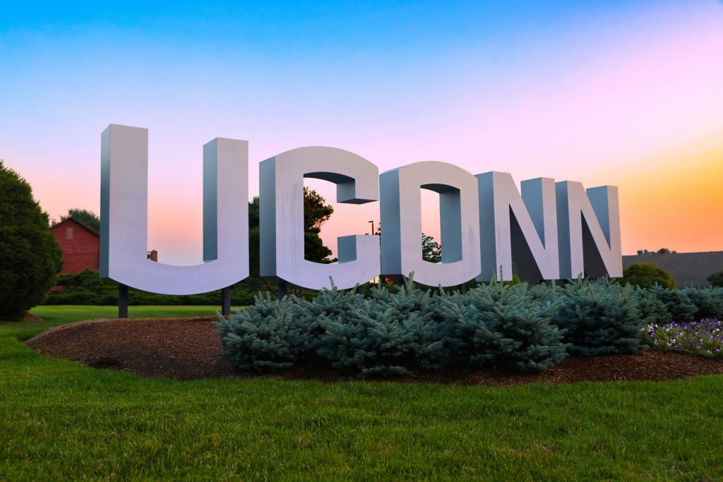The UConn sign at sunset. with various shades of blue, purple, and orange in the sky