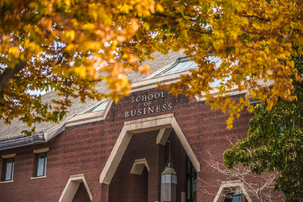 The exterior of the School of Business building, framed by tree branches with bright autumn leaves