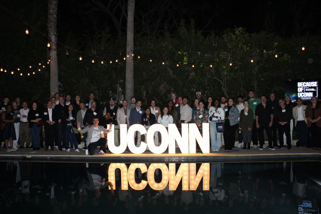 A group of UConn alumni at an event in California, standing around an illuminated "UConn" sign